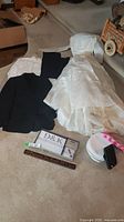 Full view of the wedding dress laid out beside tuxedo jacket, pants, shirt, and miscellaneous wedding items on carpeted floor.