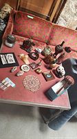 Variety of vintage collectibles arranged on a reddish table with patterned couch in background
