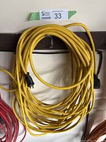 Coiled long yellow extension cord hanging on a wall hook, showing both male and female ends.