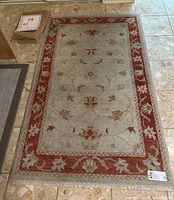 Full view of the rectangular Turkish area carpet showing beige center and rust floral border.