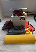 Overall photo showing all camping gear items grouped together on floor: coolers, jug, rope, bags, mattress pad, and clothing.