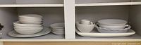 Wide view showing stacked plates, bowls, cups, and bakeware in cabinet