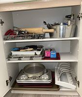Shelved cabinet with assorted cookware, bakeware including metal pans, muffin tin, and metal wire drying rack