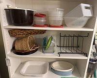 Shelf with large brown mixing bowl, plastic storage containers with lids, white plastic woven basket, woven baskets, black metal rack, and two CorningWare baking dishes