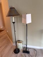 View of two floor lamps side by side against wall showing bases, columns, cords, and lampshades