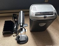 Paper shredder alongside desk lamp and metal file organizers on carpet floor.