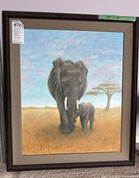 Framed painting showing full image of two elephants with grassy plains and tree background.