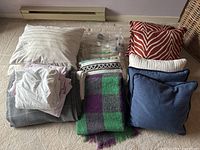 Photo showing the full assortment of pillows, blankets, and linens neatly arranged on a carpeted floor.