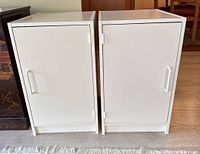 Two small white cabinets placed side by side showing front doors with handles