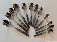 Full set of 12 polished spoons with Viking-themed handles arranged in a fan shape showing all sizes.
