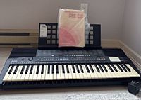 Full frontal view of Yamaha PSR-210 keyboard with owner's manual on the music stand and power adapter to the right.