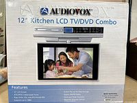 Front view of the new-in-box Audiovox 12" Kitchen LCD TV/DVD Combo packaging showing product image and key features.