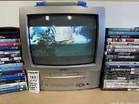 Front view of Toshiba 13-inch CRT TV displaying an image, flanked by stacks of DVD cases on either side.