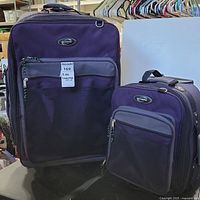 Both luggage pieces side by side showing front deep purple fabric with front zip pockets in dark grey mesh material. Olympia brand logo visible on both.
