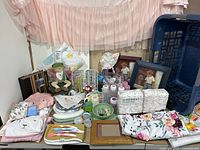 Wide photo showing all baby items including cloths, towels, bibs, bottles, diaper pack, picture frames, musical frog, floral car seat cover, crib skirt, and laundry basket