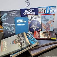 Overview photo showing all ten books arranged standing and lying down, titles visible for airplane and war-related references alongside carpentry and film books.