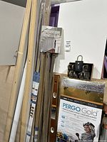 Photo showing multiple boards of white interior chair rail molding, packages of natural ginger floor molding and stair nose molding stacked vertically, with a box of 'hide a key' combination locks on top of underlayment package, and a book on interior millworker ideas hanging among the boards.
