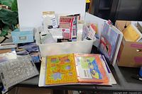 Wide view of crafting supplies showing plastic bin with various crafting and scrapbooking items, Fiskars scoring guides in binders, decorating sheets, and a small blue storage box.