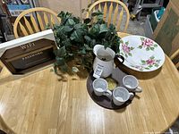 Assorted items on the oak table including placemats, mugs, pitcher, chalkboard, serving bowl, and artificial plant.