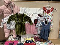 Full view of infant girl clothing items including snow suit, dresses, rompers, shirts hung on hangers