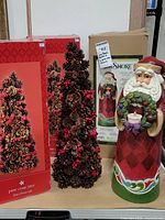 Photo showing two pine cone trees next to their original red boxes and the Jim Shore Santa's original box behind.