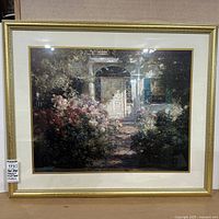 Front view of a matted and framed floral print depicting a white front door surrounded by blooming roses and other flowers. Gold-tone frame with cream matting.