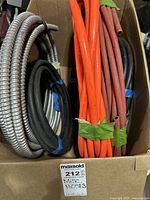 View of the multiple hoses and flexible metal conduit in cardboard box. Silver metal conduit coiled on left side, orange and red hoses bundled on right.