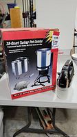 Photo of boxed 28-quart professional quality turkey pot combo with heater stand and Oster hand mixer on table.