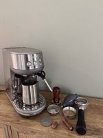 Front view of Breville Bambino espresso machine with accessories surrounding it on wooden surface