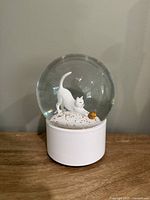 Front view of snow globe showing white cat, gold glitter, white base