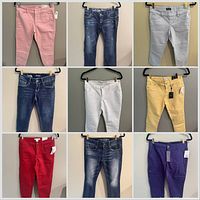 Nine pairs of jeans and pants on hangers showing front view and colour variety