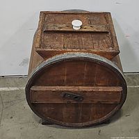 Front view of the antique wooden barrel butter churn showing the lid with a white knob and wooden handle crank on top.