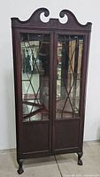 Front view of Mahoney antique corner china cabinet showing glass paneled double doors and carved wood crown.