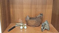 Overall view of all four items including opera glasses, magnifying glass, metal rooster sculpture, and flat iron displayed on wooden shelf.