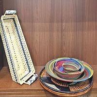 Rectangular coiled woven tray with ceramic handles next to nested multicolored round baskets