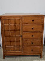 Front view of the honey-colored wooden chifforobe cabinet showing one door and five drawers with black knobs.