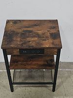 Side view of the wooden top surface and front showing built-in charging station with power outlet and USB ports, middle wooden shelf and metal mesh bottom shelf with black metal legs.