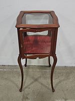 Front view of the antique curio cabinet showing its wooden frame, glass top, and single door closed.