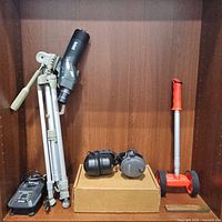 Wide view showing Ryobi ONE charger, spotting scope tripod, safety headphones, and measuring wheel.