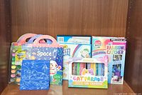 Photo of sticker books with themes including Space and Ocean Animals, Cat Parade gel crayons, 24-color watercolor paint kit, and DIY Rainbow Catcher craft kit.