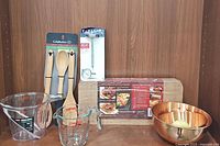 Photo showing all items together: wooden utensil set, grilling plank, measuring cups, copper bowls, meat thermometer in packaging.