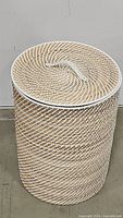 Full view of the laundry hamper with lid on, showing woven spiral pattern in beige and white with a handle on the lid.