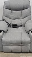 Front view of grey fabric power recliner chair with cushioned back and armrests, power cord and remote control on seat