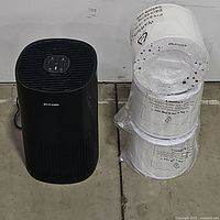 PuroAir black air purifier next to three new sealed white replacement filters on the floor.