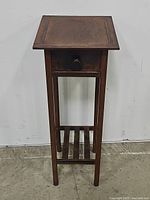 Front view of slim metal table showing drawer and slatted bottom shelf