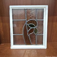 Front view of stained glass window with white wooden frame, showing leaf design and textured glass panels.