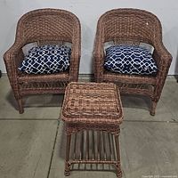 Front view of two wicker patio chairs each with a blue and white patterned cushion and a matching square wicker ottoman table.