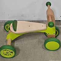 Side view showing the wooden frame with bright green parts, wheels, seat and handlebar of the Hape ride-on bike.