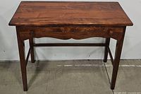 Front view of vintage wooden writing table showing overall form, drawer, and leg structure