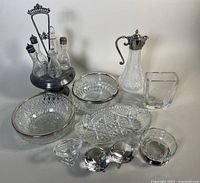 Photo of full lot showing two silver plate rimmed Vide-Poche bowls, crystal Bacchus claret jug, Art Deco cruet stand with five condiment bottles, and additional small cut crystal dishes and items.